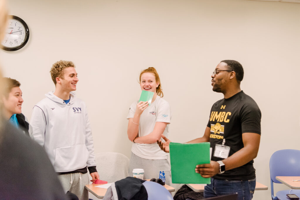 Student trainer in UMBC t-shirt (at right) chats with a small group of other UMBC students (at left).
