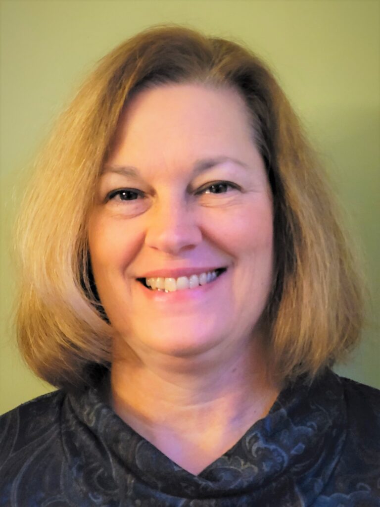 A woman with neck- length blond hair wearing a black blouse smiles at camera.