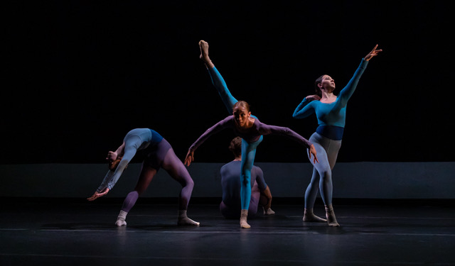 Against a dark background, four dancers perform on stage
