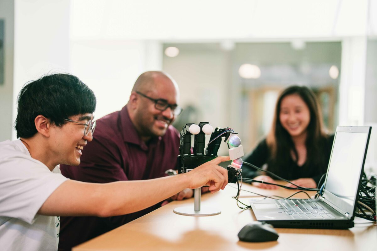 Mechanical engineering professor and students looking at a robotic fingertip developed in the lab called DenseTact that will enable robots to perform dexterous tasks like humans in the near future.