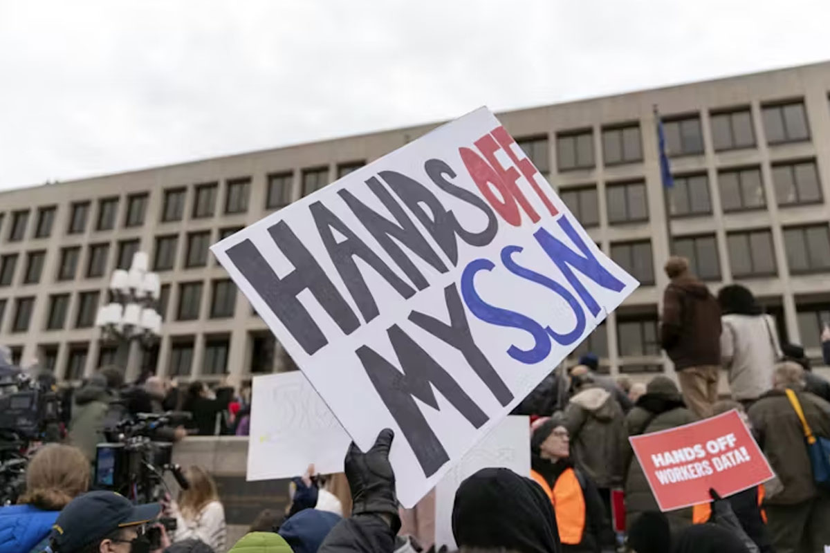 Protestors in front of building. Signs read "Hands off my SSN" and "Hands off workers data"