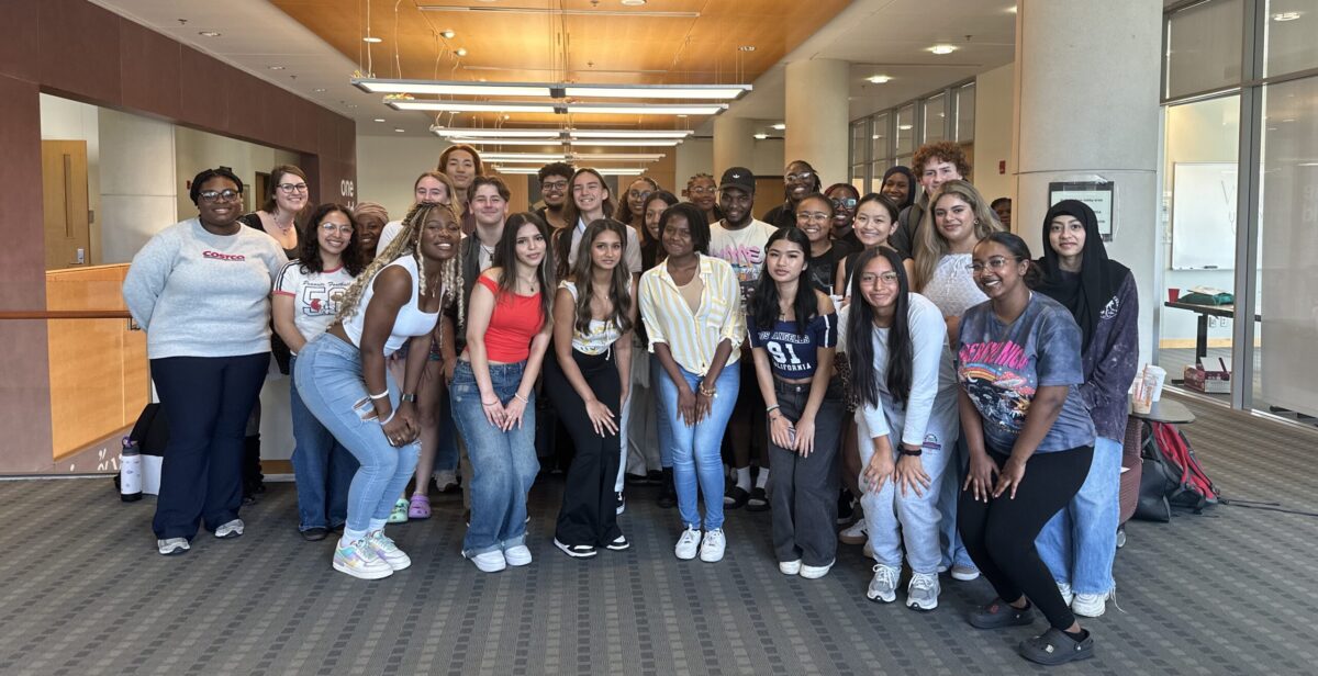 A large group of college students group in a carpeted hallway for a picture