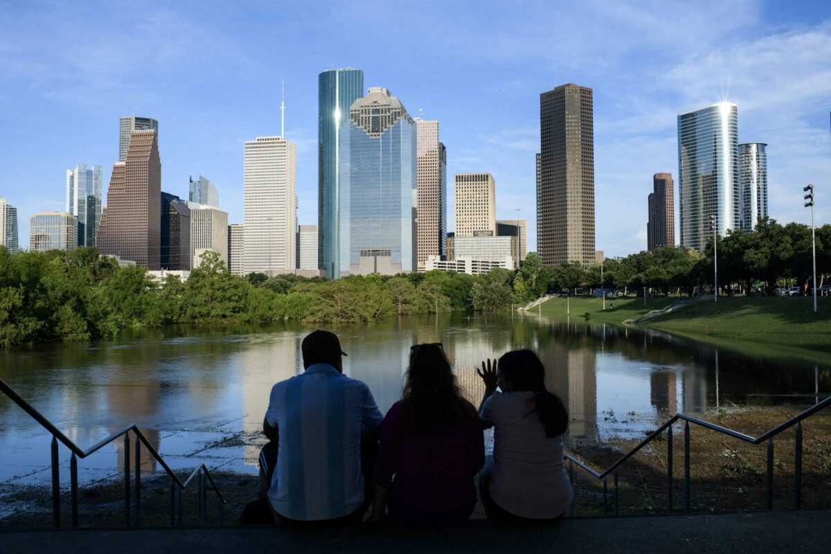 A group of three people sitting by a lake overlooking a city landscape