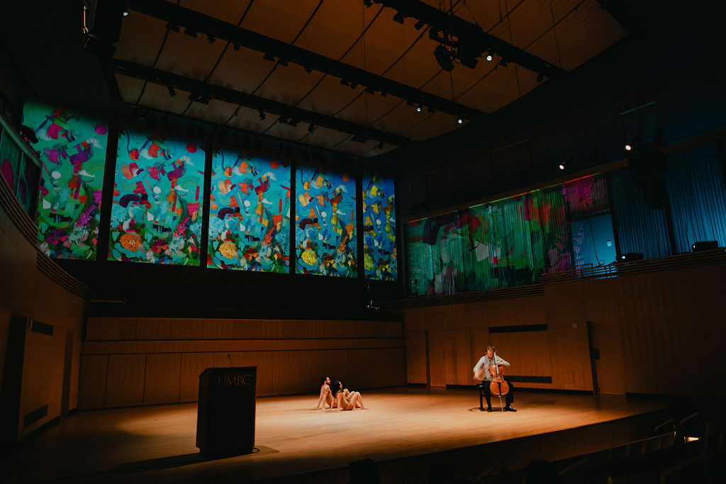two people dance on stage while someone plays the cello