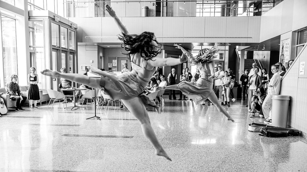a black and white photos of dancers jumping in an atrium