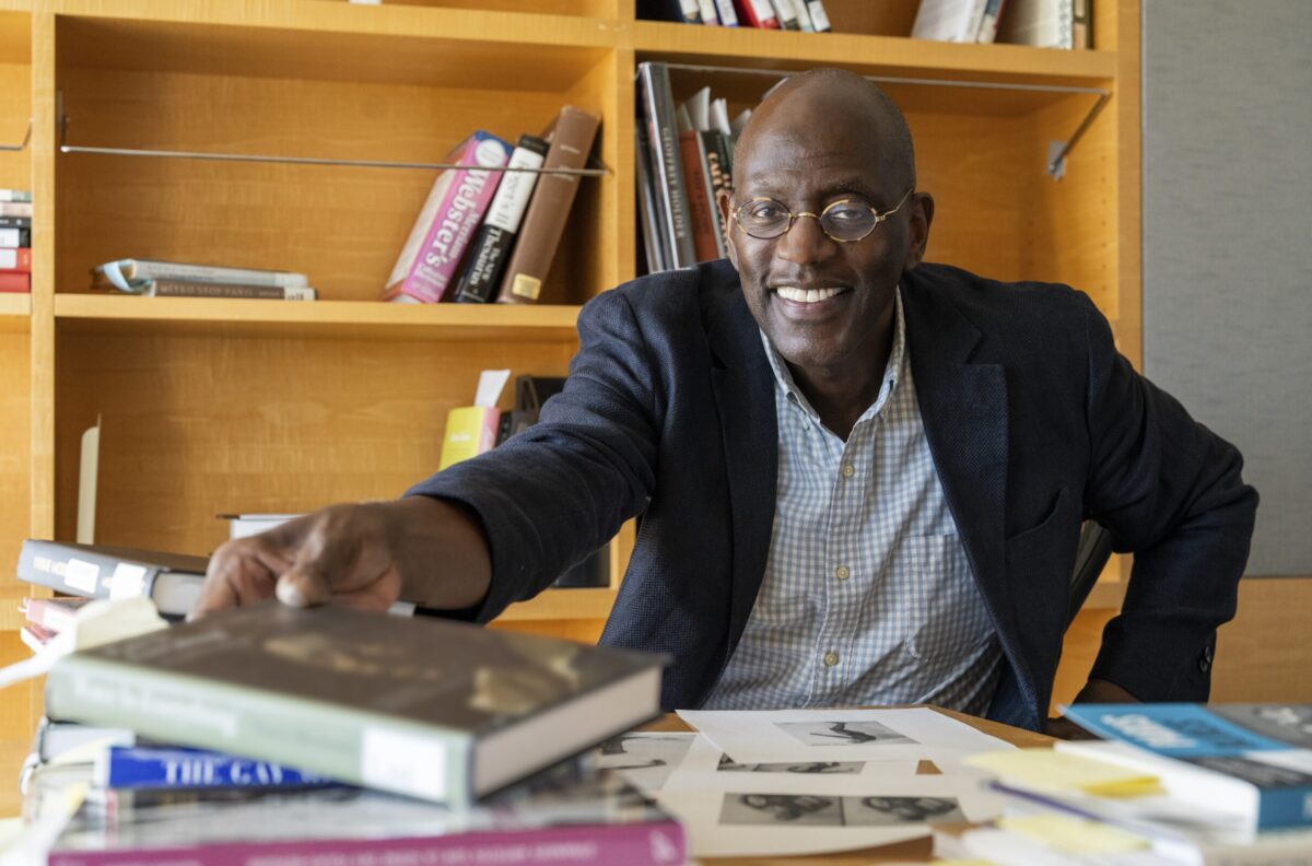 James Smalls, a visual arts professor, sits at his desk surrounded by books about Féral Benga with a book shelf behind him