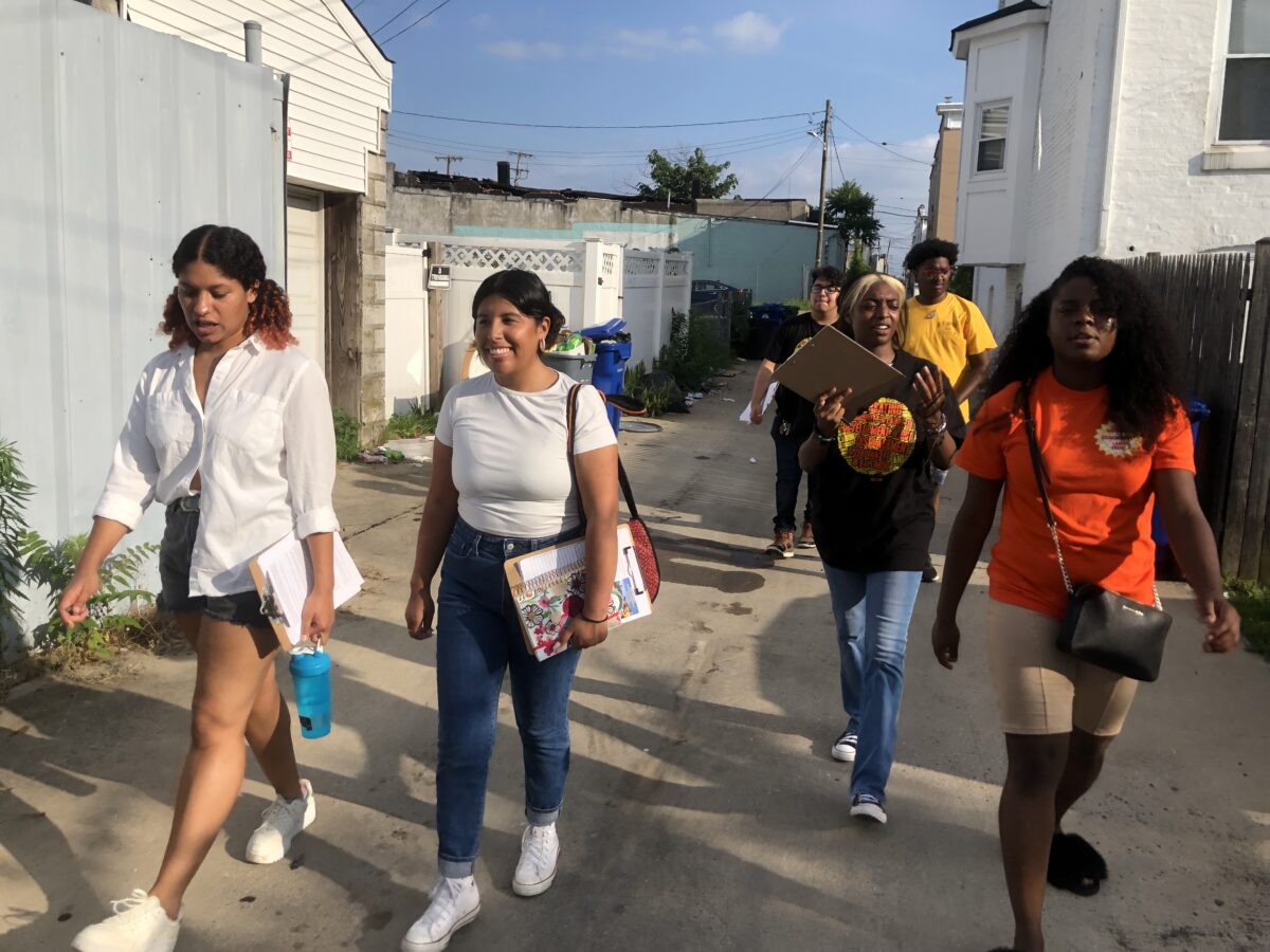 several people walk through a neighborhood, one carrying a clipboard
