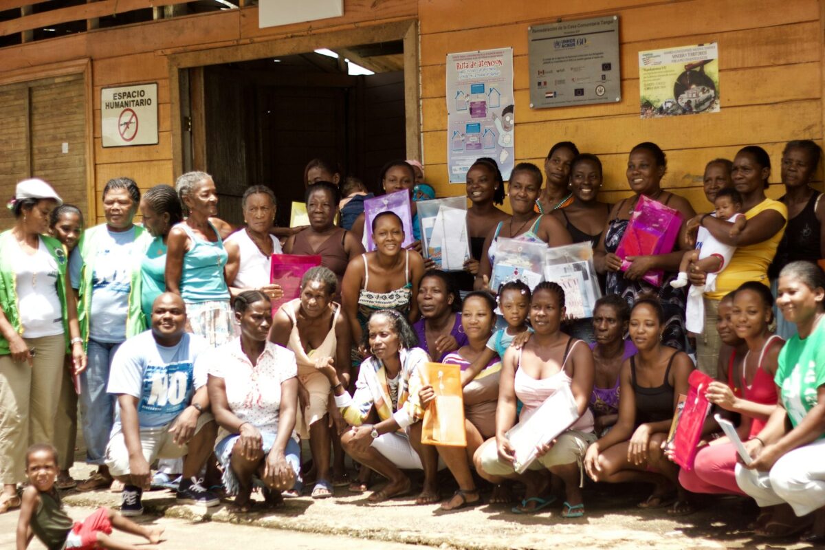 A large group of Afro-Colombian women kneel and stand for a photo in front of a yellow building